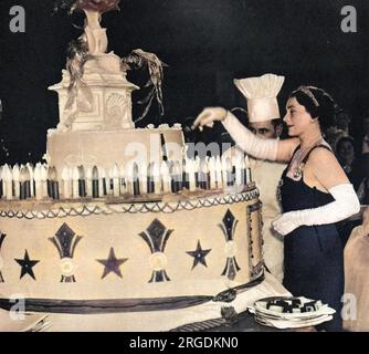La Duchessa di Gloucester (1901-2004) tagliò la torta gigante contenente 194 candele elettriche che rappresentano il numero di anni dalla nascita della Regina Carlotta al ballo che prese il suo nome. Il Queen Charlotte's Ball, tenuto in onore della moglie di re Giorgio III e ripreso nel 1925 per raccogliere fondi per l'omonimo ospedale di maternità è stato uno dei momenti salienti della stagione londinese per un debuttante. Tutte le ragazze erano vestite di bianco, e si immergevano in una ricciola attentamente coreografata mentre la torta veniva tagliata. A quanto pare, c'era un bel tifo per prendere un pezzo di torta dopo! Foto Stock