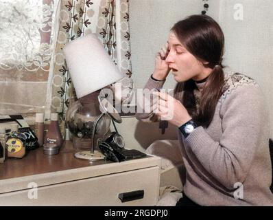 Una giovane donna mette il suo trucco al suo tavolo da spogliatoio della camera da letto. Foto Stock