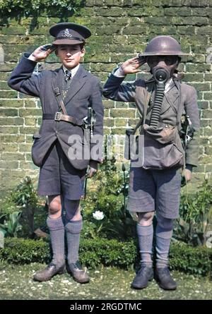 Due ragazzi salutano, probabilmente durante la seconda guerra mondiale. Quello a destra indossa un casco di latta e una maschera a gas. Quello a sinistra indossa un berretto di artiglieria reale e una spada cerimoniale. Foto Stock