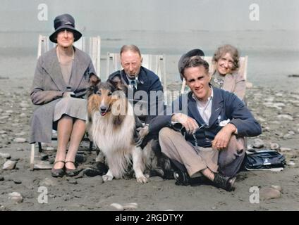 Quattro persone (due uomini e due donne) sedute in sdraio su una spiaggia con un cane collie. Foto Stock