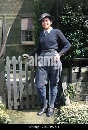 Un membro dell'Esercito terrestre delle Donne (ragazza di terra) durante la seconda guerra mondiale, in piedi accanto a un cancello del giardino. Foto Stock