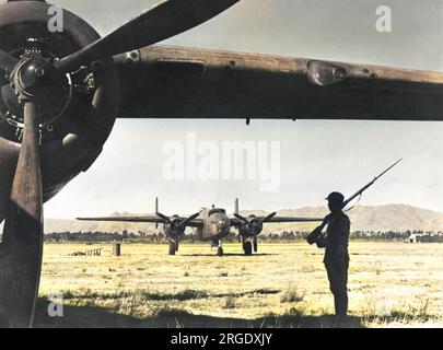 Una sentinella cinese sta di guardia all'ombra dell'ala di un bombardiere della 14th U.S. Army Air Force in un aerodromo in Cina. Sullo sfondo c'è un altro bombardiere pronto per decollare in una missione contro i giapponesi Foto Stock