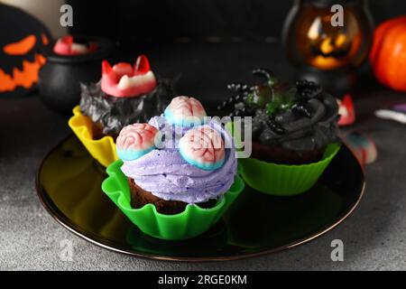 Piatto con deliziosi cupcake e caramelle di Halloween su sfondo scuro, primo piano Foto Stock