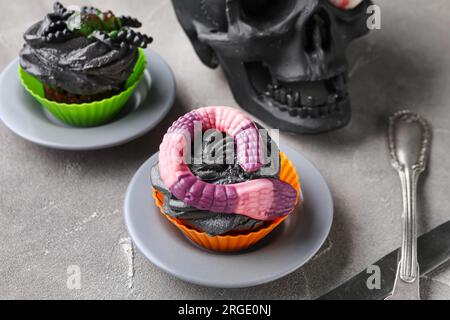 Cranio e deliziosi cupcake di Halloween su sfondo grigio, primo piano Foto Stock