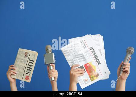 Mani femminili con microfoni e giornali su sfondo blu Foto Stock