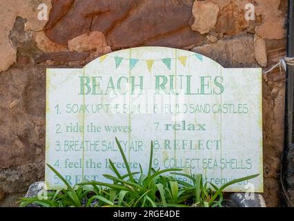 Divertente cartello su un muro in un villaggio costiero con regole umoristiche sulla spiaggia Foto Stock