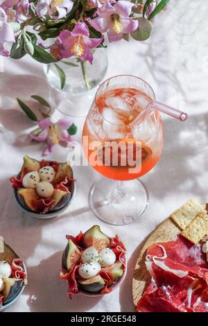 cocktail aperol spritz, su una tovaglia di lino rosa pallido, ombre, luce del sole, drink estivo in bicchiere Foto Stock