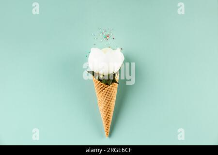 Creativi nature morte di cono waffle con fiore di peonia su sfondo blu pastello, vista dall'alto. Minimalista per l'estate Foto Stock