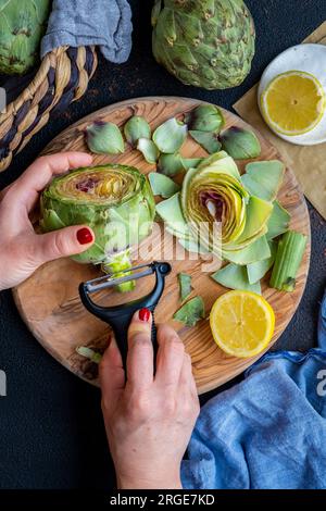 Le mani di una donna pelano il gambo di un carciofo usando una pelatrice. Foto Stock