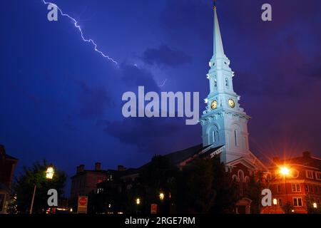 Un fulmine lampeggia nel cielo vicino a una chiesa storica con un campanile illuminato nel New England, creando una scena spaventosa e spaventosa Foto Stock