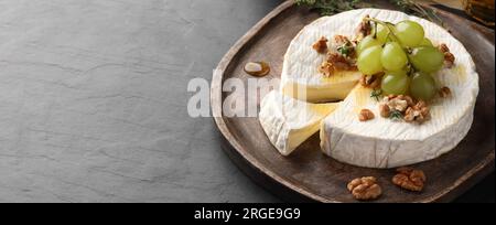 Gustoso formaggio brie con uva, noci e miele su tavola grigia, spazio per testo. Design banner Foto Stock
