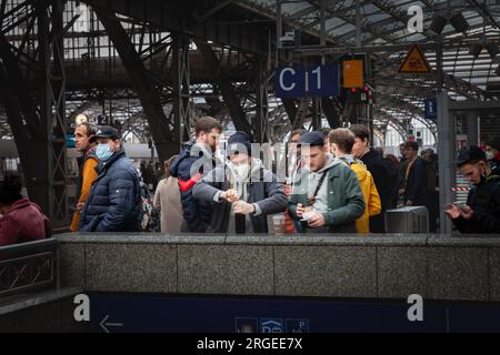 Immagine degli uomini in attesa di un treno sulle piattaforme della stazione ferroviaria di Koln hauptbahnhof, indossando maschere facciali durante il Coronavirus Covid 19 salute cris Foto Stock