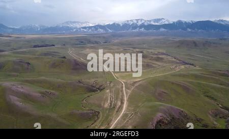 Strada tra le colline di montagna. Sullo sfondo di montagne innevate. Vista da un drone Foto Stock