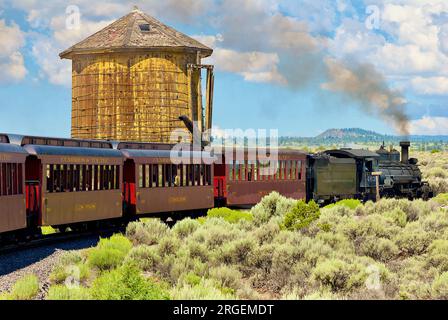 Antonito, Colorado, USA - 22 luglio 2023: La Cumbres and Toltec Scenic Railroad passa accanto a un serbatoio d'acqua originale della Denver & Rio grande Railroad. Foto Stock