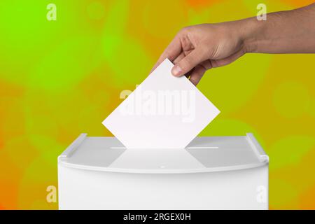 Uomo che mette il suo voto nelle urne su sfondo a colori, primo piano Foto Stock