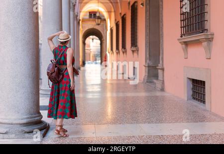 Giovane turista vestita casualmente in piedi con cappello nelle famose gallerie ad arco della città di Bologna in Italia. Bologna è una città studentesca e sede di t Foto Stock