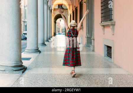 Giovane studentessa vestita casualmente in piedi a braccia aperte nelle famose gallerie ad arco della città di Bologna in Italia. Bologna è città studentesca e hom Foto Stock