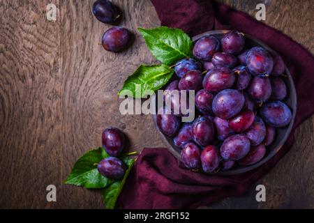 Prugne fresche sul piatto su sfondo di legno scuro Foto Stock