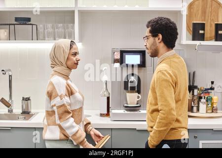 Ritratto laterale di due colleghi del Medio Oriente, uomo e donna, che parlano in ufficio in piedi accanto alla postazione caffè Foto Stock