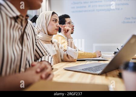 Vista laterale ritratto di uomini d'affari arabi seduti a un tavolo in fila durante una riunione o un seminario, attenzione su una donna che indossa il velo, spazio fotocopie Foto Stock