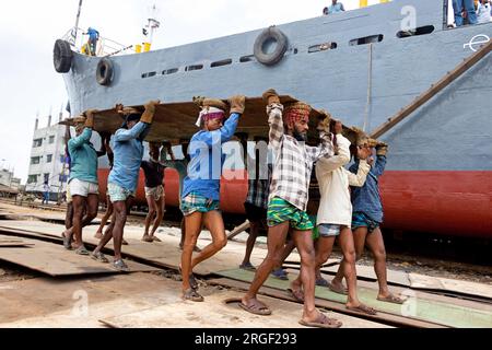 Dhaka, Dhaka, Bangladesh. 9 agosto 2023. Un gruppo di portatori trasporta una pesante piastra di acciaio di 250 kg in un cantiere navale sulla riva del fiume Buriganga, a Keraniganj, vicino a Dacca, Bangladesh. Dozzine di cantieri che occupano 30,96 acri della costa di Buriganga sono stati in funzione negli ultimi 50 anni. Viene utilizzato principalmente per riparare e riparare vecchie navi e costruire nuove navi. Le maestranze lavorano nel cantiere senza caschi, maschere facciali o scarpe di sicurezza. Lavorano sodo tutto il giorno, ma sono ancora pagati salari minimi. Con un numero crescente di ordini da parte di acquirenti sia locali che globali, il cantieristico Foto Stock