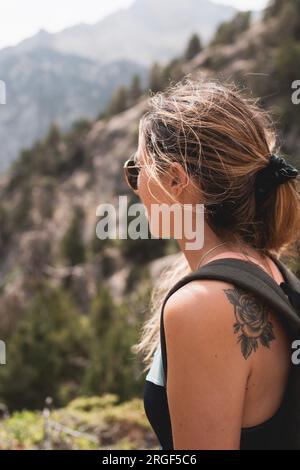 primo piano di una giovane donna bionda, che indossa occhiali da sole guardando il paesaggio dei Pirenei in estate Foto Stock