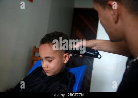 salvador, bahia, brasile - 27 agosto 2022: barber utilizza una macchina per tagliare i capelli di un bambino nella città di Salvador. Foto Stock