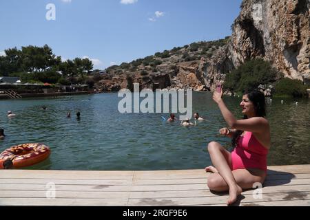 Vouliagmeni Atene Grecia donna che si prende un Selfie sul suo smartphone e turisti nuotare nel lago Vouliagmeni una spa naturale - una volta era una caverna ma il Foto Stock