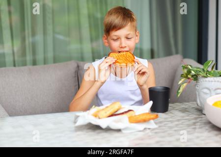 Il ragazzo fa la colazione dolce al tavolo in cucina. Foto Stock