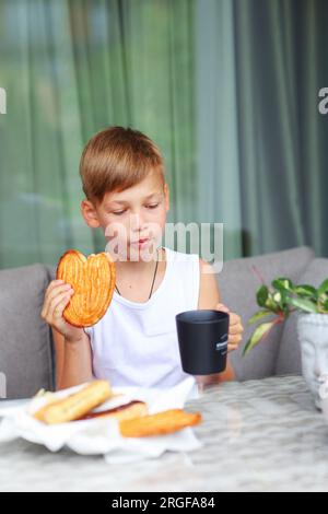 Il ragazzo fa la colazione dolce al tavolo in cucina. Foto Stock