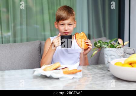 Il ragazzo beve il tè con la colazione dolce al tavolo in cucina. Foto Stock