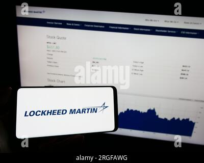 Persona che possiede un telefono cellulare con il logo della società di difesa statunitense Lockheed Martin Corporation sullo schermo davanti alla pagina Web. Concentrarsi sul display del telefono. Foto Stock