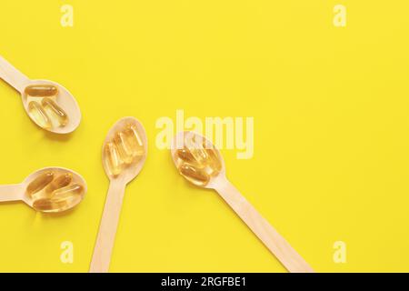 Omega 3. Capsule dorate con olio di pesce in cucchiai di legno su sfondo giallo, vista dall'alto. Industria farmaceutica. Assistenza sanitaria e medicina. pr. Farmacia Foto Stock