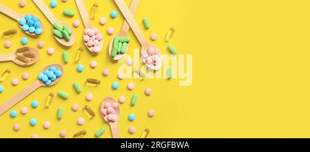 Vitamine di diversi colori in cucchiai di legno su sfondo giallo. Vista dall'alto delle pillole luminose sparse. Industria farmaceutica. Sanità e medicina Foto Stock