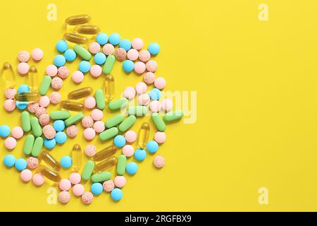 Vitamine di colori diversi su sfondo giallo. Vista dall'alto di un mucchio di pillole luminose. Industria farmaceutica. Assistenza sanitaria e medicina. Farmacia Foto Stock