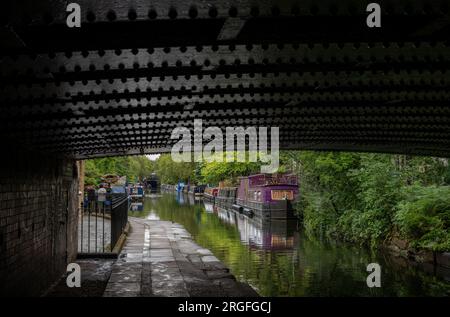 Londra, Regno Unito: Case galleggianti a Blomberg Road Moorings sul Regent's Canal a Londra, parte dell'area conosciuta come Little Venice. Visto da sotto un ponte. Foto Stock