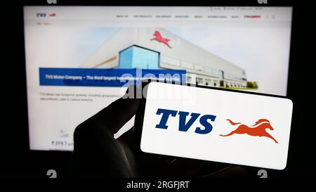 Persona che possiede uno smartphone con il logo dell'azienda di motociclette TVS Motor Company Limited sullo schermo di fronte al sito Web. Concentrarsi sul display del telefono. Foto Stock