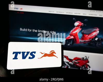 Persona che possiede il cellulare con il logo dell'azienda di motociclette TVS Motor Company Limited sullo schermo davanti alla pagina Web. Concentrarsi sul display del telefono. Foto Stock