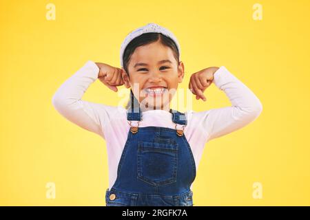 Sorridi, ritratto e bambina con braccio flessibile in studio per sicurezza, forza e potenza su sfondo giallo. Felice, faccia ed eccitato ragazzo con bicipite Foto Stock