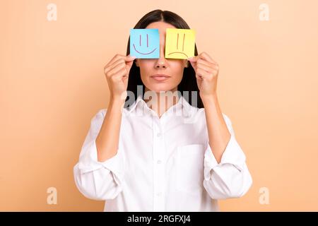 Ritratto di persona calma e seria braccia con due adesivi per appunti di carta emoji felice triste isolato su sfondo di colore beige Foto Stock