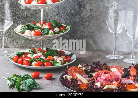 Insalata italiana classica insalata caprese e un piatto con una selezione di specialità di salsiccia su sfondo grigio Foto Stock