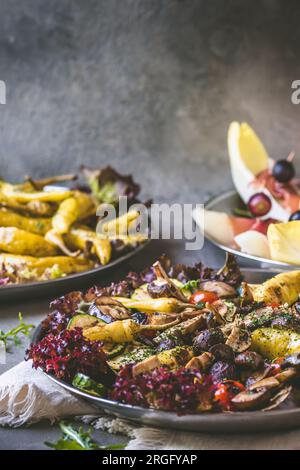 Buffet di antipasti italiani con verdure alla griglia, peperoni alla griglia e melone avvolti con prosciutto su sfondo grigio, verticale con spazio copia Foto Stock