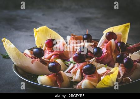 Melone dolce avvolto con prosciutto, antipasto italiano, su sfondo rustico grigio, spazio copia Foto Stock