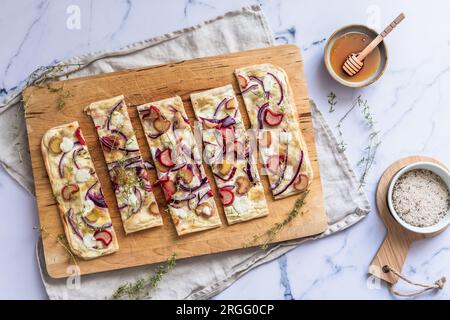 Tarte flambee al forno con rabarbaro, cipolle rosse, formaggio di capra e miele, tagliate a strisce, sfondo di marmo, vista dall'alto Foto Stock