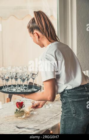 La giovane cameriera mette i tavoli nel ristorante con bicchieri, verticali Foto Stock