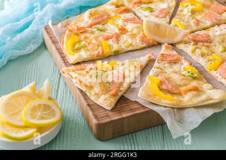 Pezzetti di fiammato con salmone, pepe giallo e cipolline su un asse di legno su sfondo verde chiaro Foto Stock