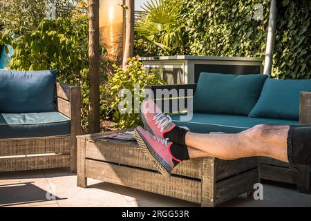 Accogliente area salotto ombreggiata con mobili in legno, un uomo mette le gambe sul tavolo per rilassarsi Foto Stock