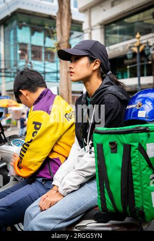 Un corriere thailandese si siede con la sua amica sulla sua bici facendo una pausa sulla sala Daeng Rd. Bangkok, Thailandia. Foto Stock