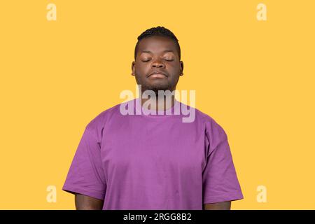 Tired Black Guy che posa sonnolento con gli occhi chiusi, sfondo giallo Foto Stock