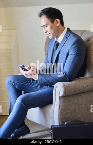 Imprenditore utilizzando smart phone in hotel room poltrona Foto Stock